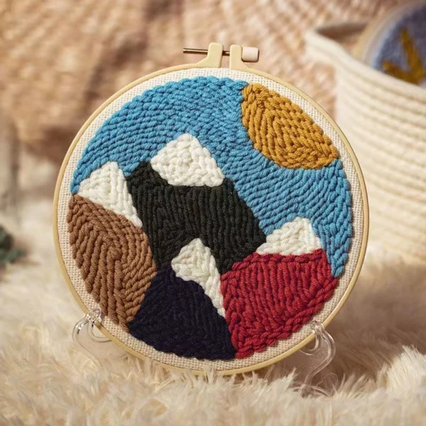 Layered peaks punch needle art kit with geometric mountain silhouettes in wooden hoop, yarn, and beginner crafting tools