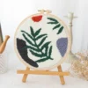 Punch needle embroidery kit featuring wild leaves botanical pattern in wooden hoop with green yarns and crafting tools for beginners