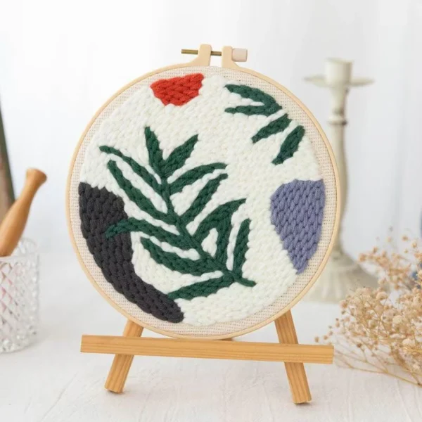 Punch needle embroidery kit featuring wild leaves botanical pattern in wooden hoop with green yarns and crafting tools for beginners