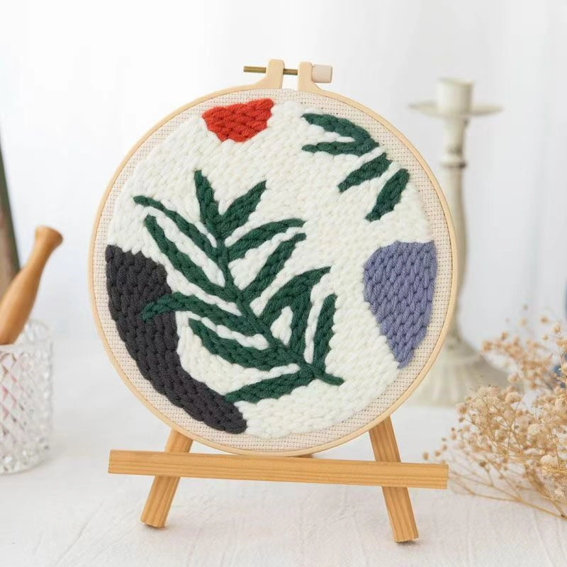 Punch needle embroidery kit featuring wild leaves botanical pattern in wooden hoop with green yarns and crafting tools for beginners