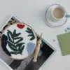 Punch needle embroidery wild leaves design displayed with coffee cup and magazines in cozy lifestyle crafting scene