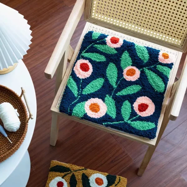 Blue floral punch needle pillow on wooden chair, featuring handmade texture and vibrant colors.