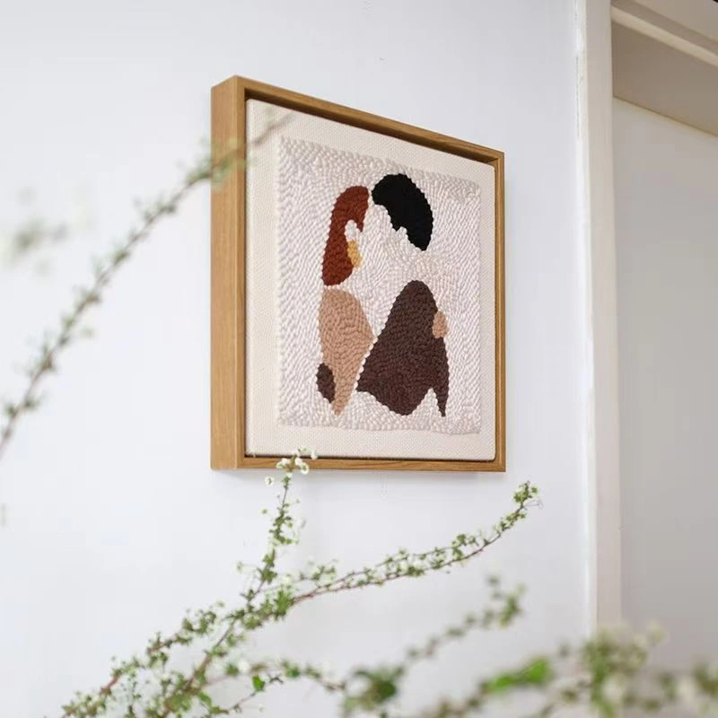Close-up of DIY couple gift framed punch needle art showing brown and black abstract couple figures on textured fabric