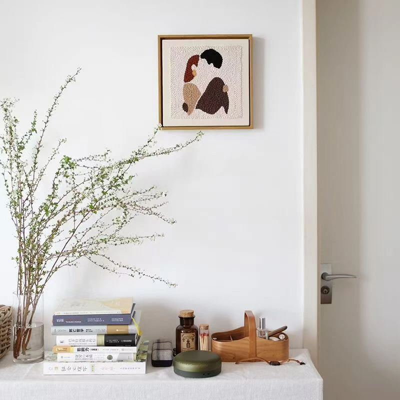 DIY couple gift punch needle wall art hung above desk with books and plants in minimalist modern room decor
