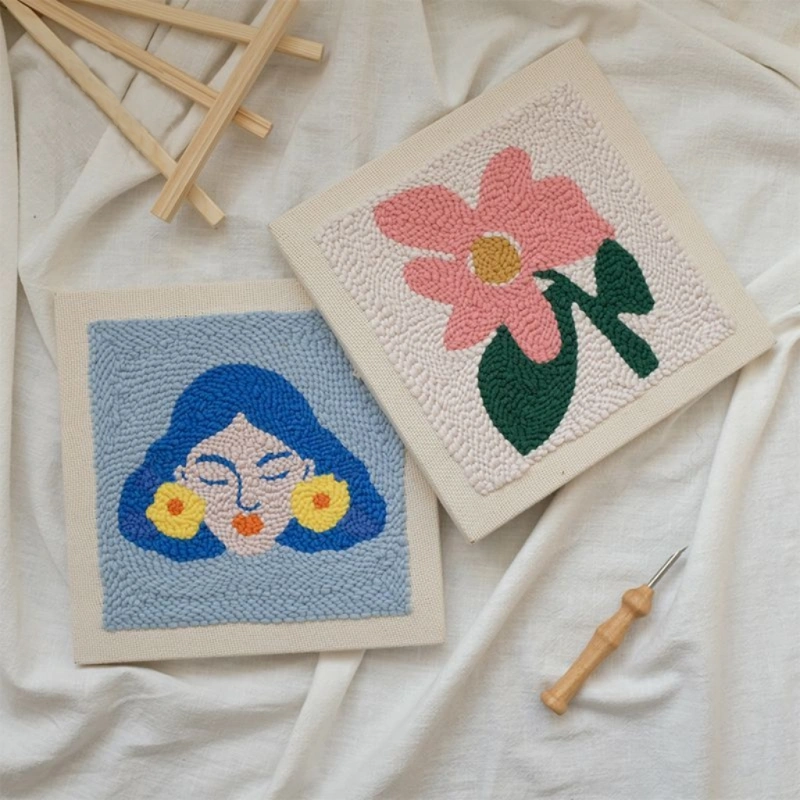Wall art punch needle kits of Frida Kahlo with blue portrait and pink flower design, crafting tools on white fabric