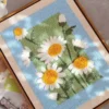 Finished daisy punch needle wall art with white petals and yellow centers, framed with blue and green background.