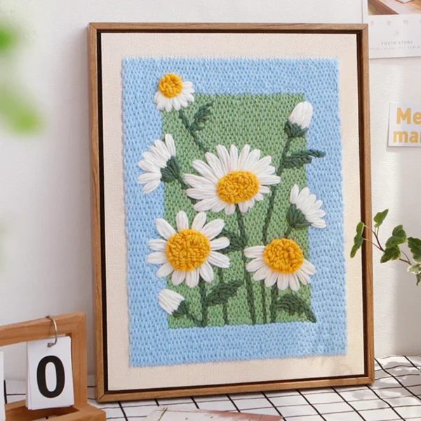Framed punch needle daisy wall art with white and yellow flowers, displayed on a wall.