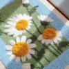 Close-up of punch needle daisy wall art in sunlight, showing vibrant texture and handmade detail.