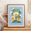 Framed daisy punch needle artwork displayed on table, adding cozy charm to home decor.