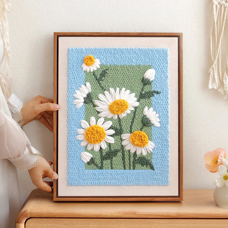 Framed daisy punch needle artwork displayed on table, adding cozy charm to home decor.