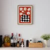 DIY wall decor punch needle art showing black checkered vase with white flowers on red fabric, framed and displayed above bar area