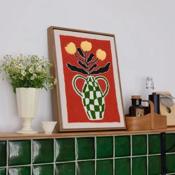 Framed punch needle wall art with a green vase and yellow flowers in bold colors on a red background.