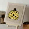 Yellow polka dot pumpkin punch needle art on beige canvas displayed on wooden easel