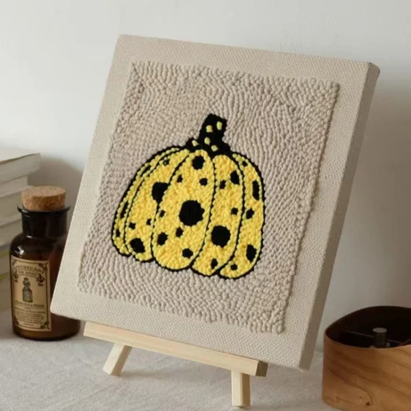 Yellow polka dot pumpkin punch needle art on beige canvas displayed on wooden easel