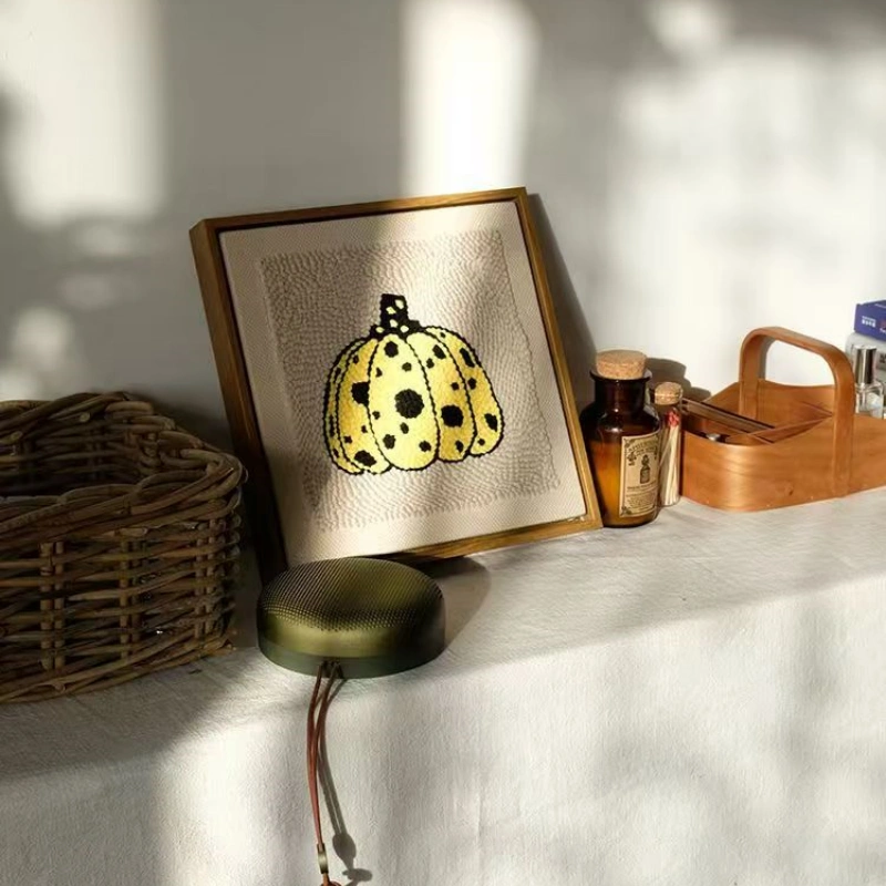 Framed yellow spotted pumpkin punch needle artwork in golden frame on white table