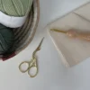 Gold stork embroidery scissors with ornate design on white surface beside yarn and fabric, premium crafting tools