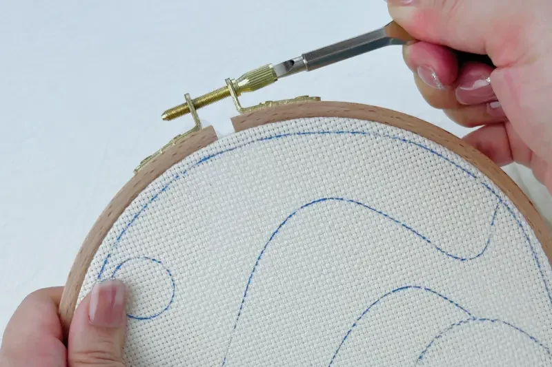 Tightening the hoop screw with a flat head screwdriver to secure the fabric.