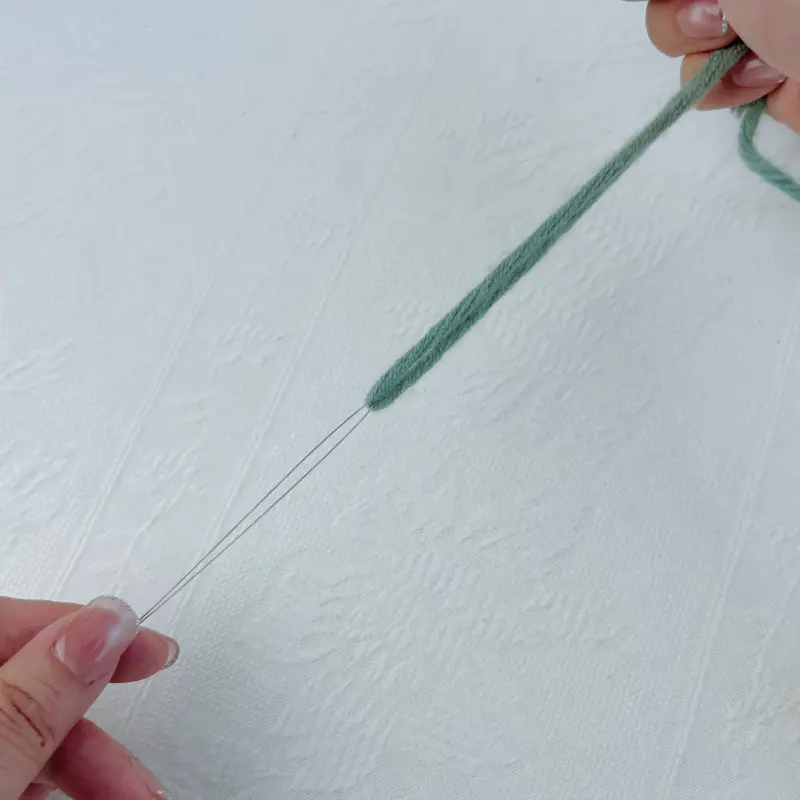 Threading green yarn through the loop of the needle threader, holding both ends of the threader by hand.